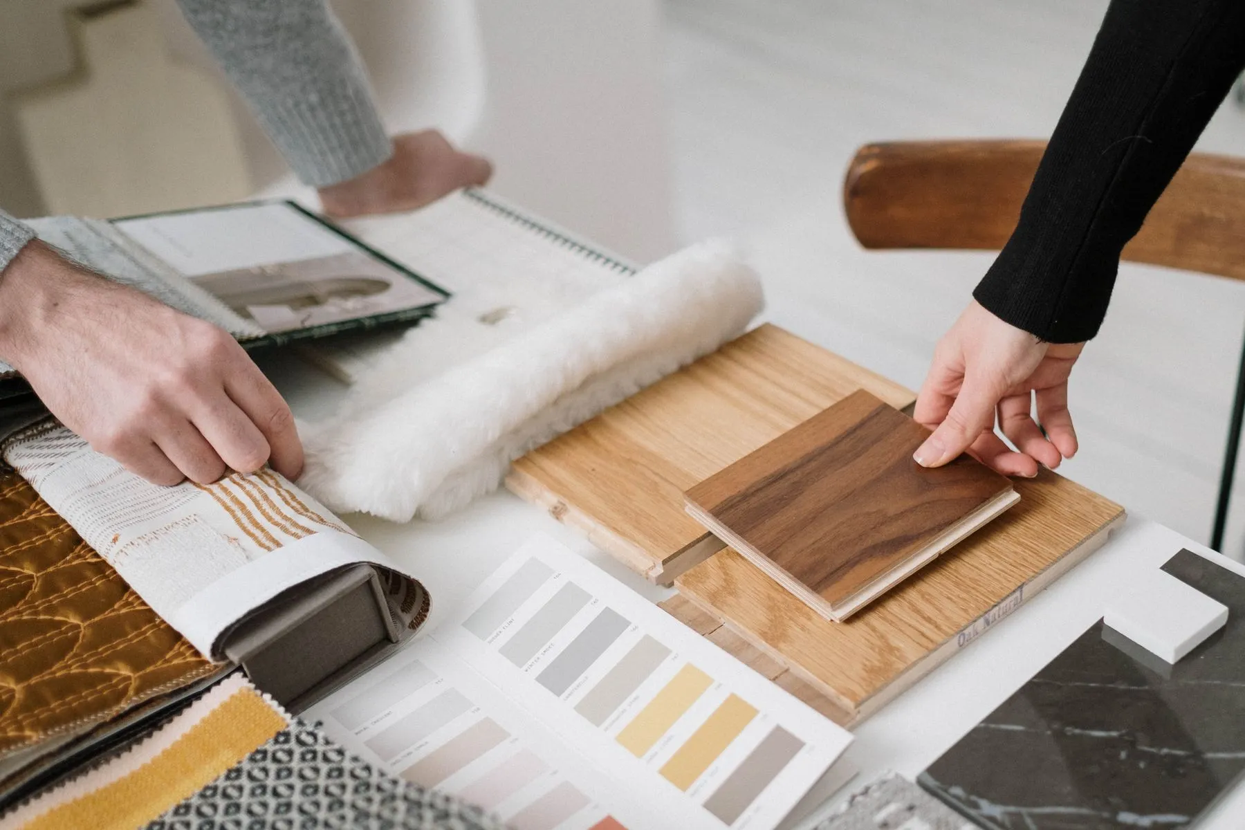 Two people comparing oak and walnut flooring samples on a table