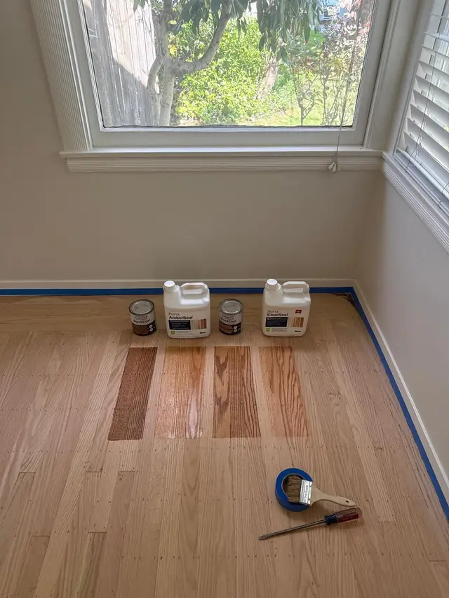 Wood stain color samples on sanded oak floor during hardwood refinishing