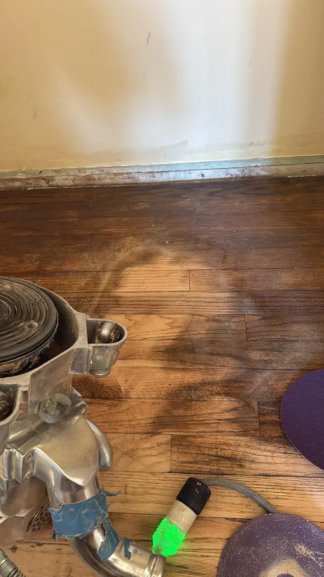 Hardwood floor refinishing in progress with a sander removing old dark stain from oak