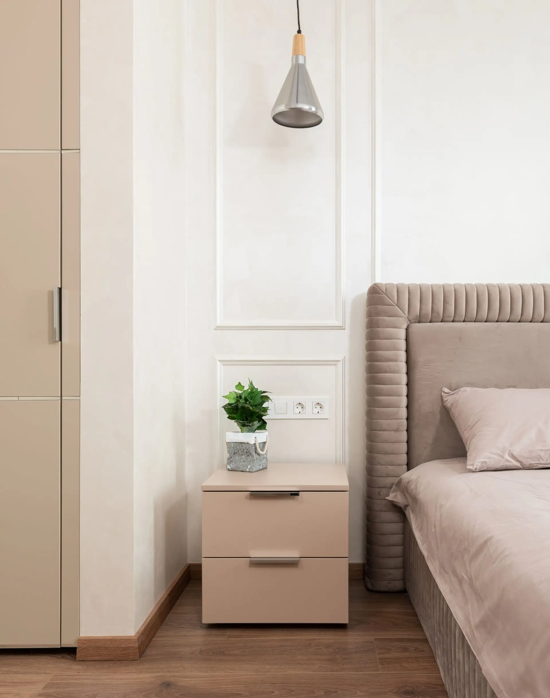 Bedroom corner with dark plank flooring and a beige nightstand