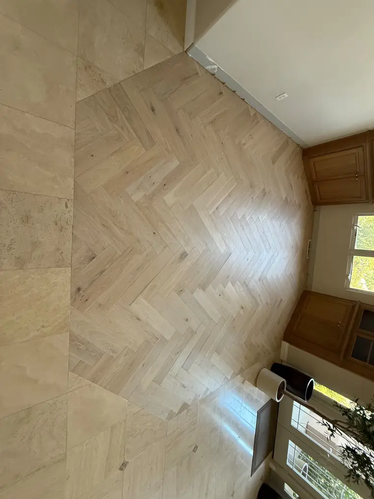 After: Bare plywood subfloor transformed with a herringbone oak pattern meeting travertine tile