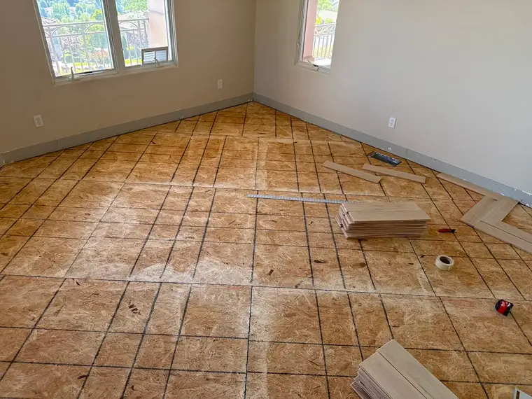 Before: Bare plywood subfloor transformed with a herringbone oak pattern meeting travertine tile