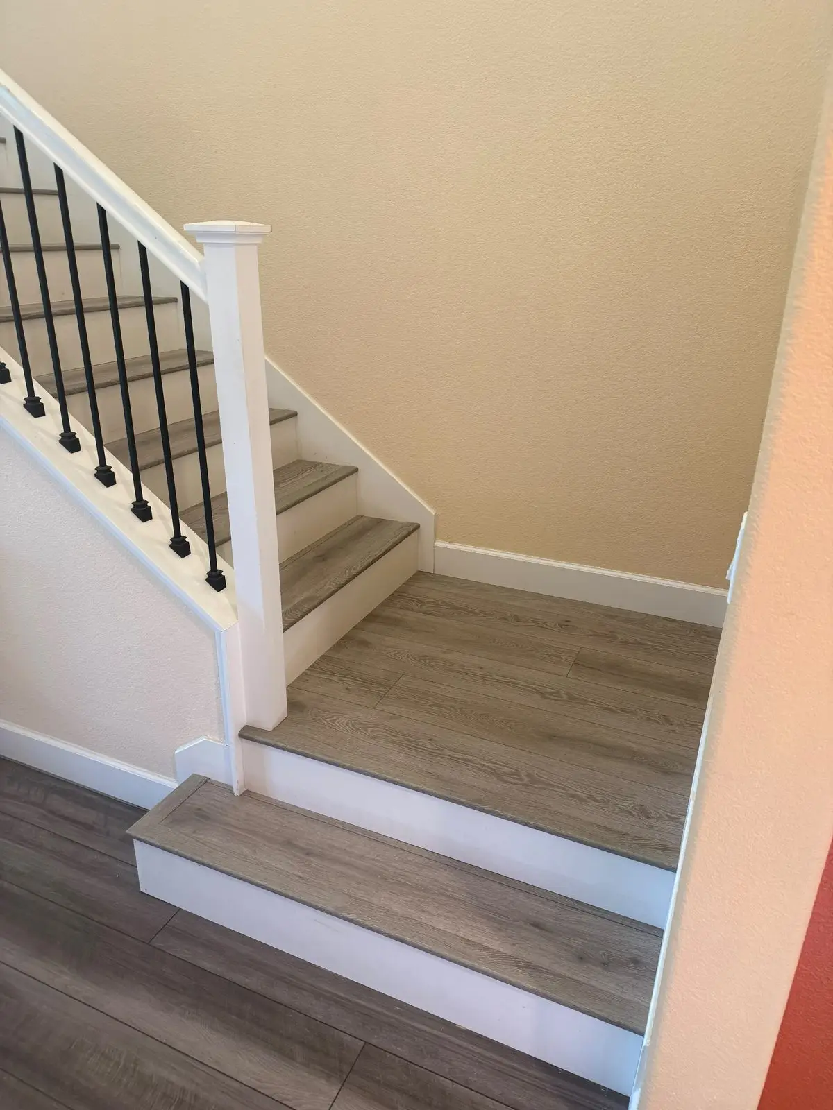 Staircase landing finished with grey oak look plank treads, white risers and black metal balusters in a Folsom home